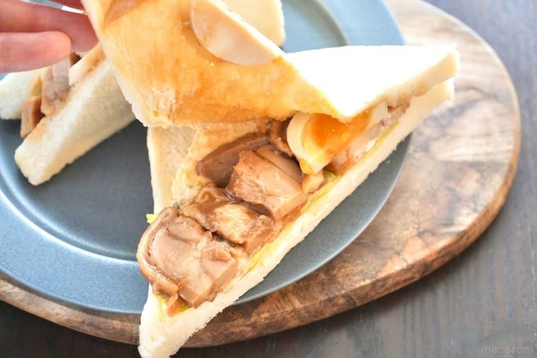 木のカッティングボードとグレーの皿にのった照り焼きチキン入りのサンドイッチをめくる様子とストライプの布