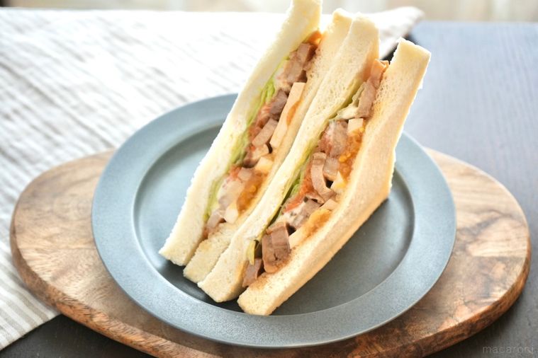 木のカッティングボードとグレーの皿にのった照り焼きチキン入りのサンドイッチとストライプの布