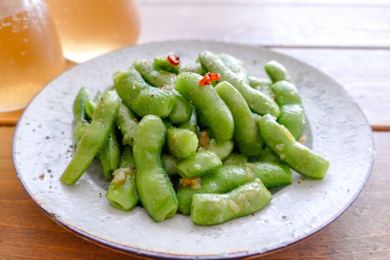 枝豆ペペロンを盛り付けた皿とビールが置かれた木製テーブル