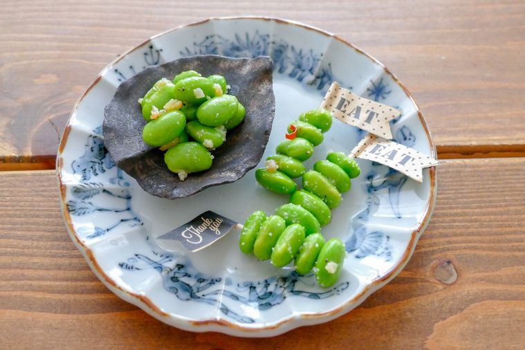 小皿に盛り付けたむき枝豆ペペロンと、ピックに刺したむき枝豆ペペロン