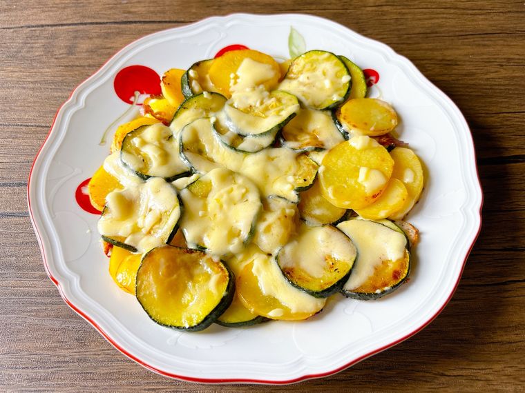 赤色の縁取りの丸皿に盛られたズッキーニ、じゃがいも、チーズのフライパン蒸し