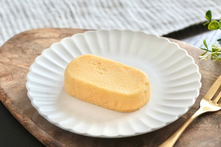 木のカッティングボードと白い皿にのった泡食感のチーズケーキと金のフォークとストライプの布とグリーン