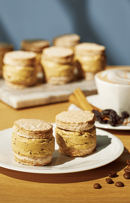 木製のテーブルの上に白いお皿にのったダックワーズサンドやカフェラテなどが置いてある