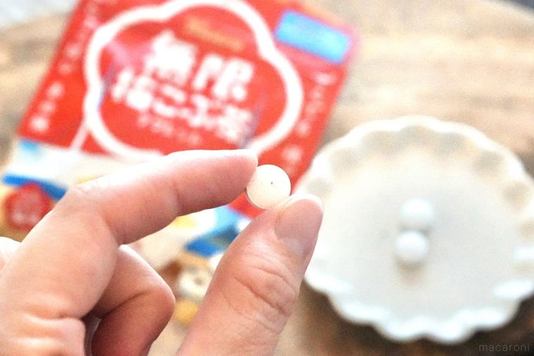 木のカッティングボードにのった白い小皿と赤いパッケージと梅こぶ茶味のタブレットを手に持つ様子