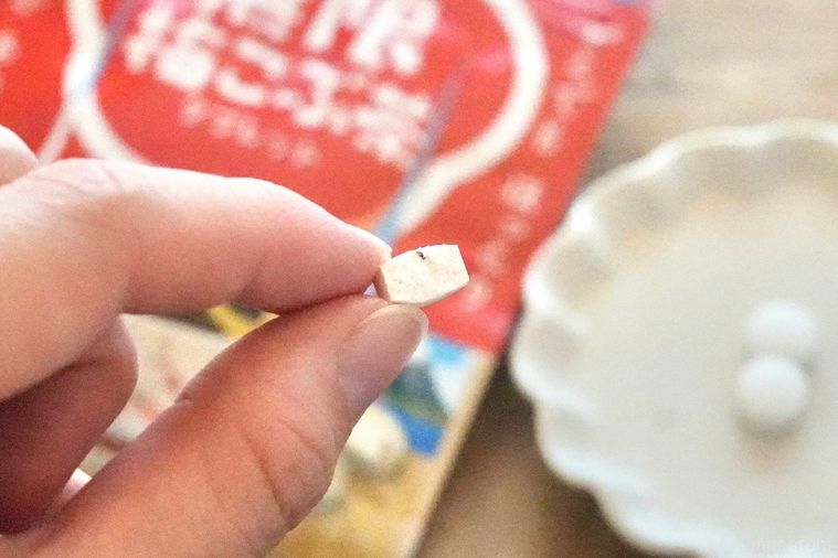 木のカッティングボードにのった白い小皿と赤いパッケージと梅こぶ茶味のタブレットを手に持つ様子