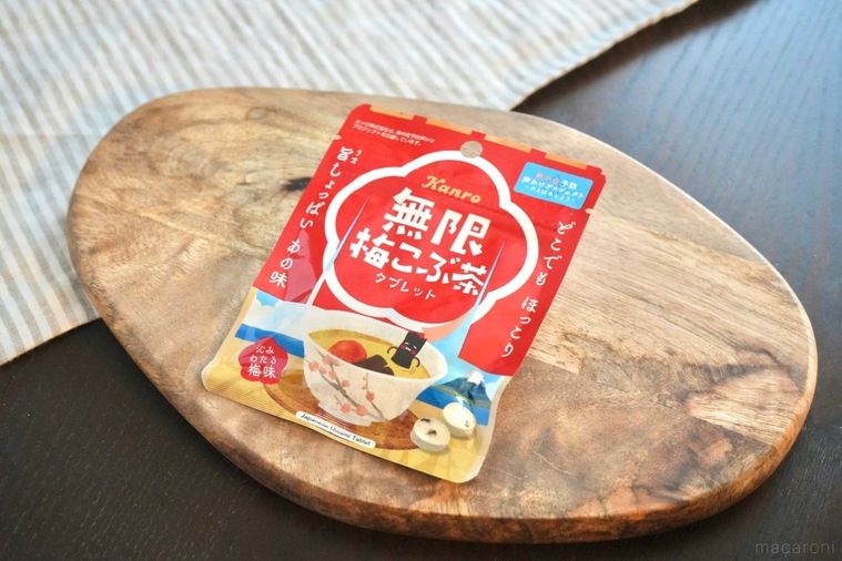 木のカッティングボードにのった梅昆布茶味のタブレットの赤いパッケージとストライプの布