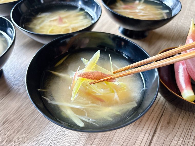 黒色のお椀に入った味噌汁のみょうがを箸で持ち上げた様子