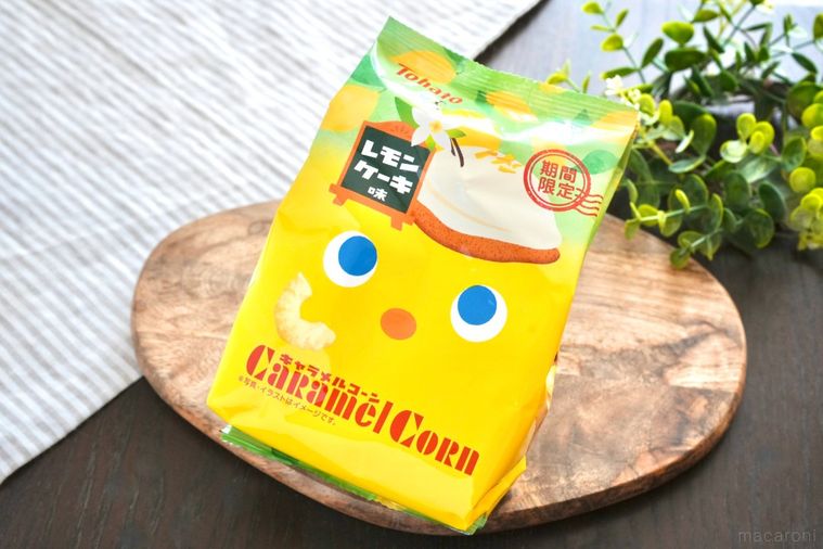 木のカッティングボードにのったレモンケーキ味のキャラメルコーンの黄色いパッケージとストライプの布とグリーン