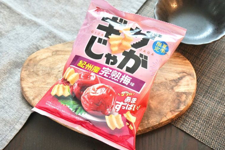 木のカッティングボードにのった梅味のポテトスナックとグレーの布と黒い器