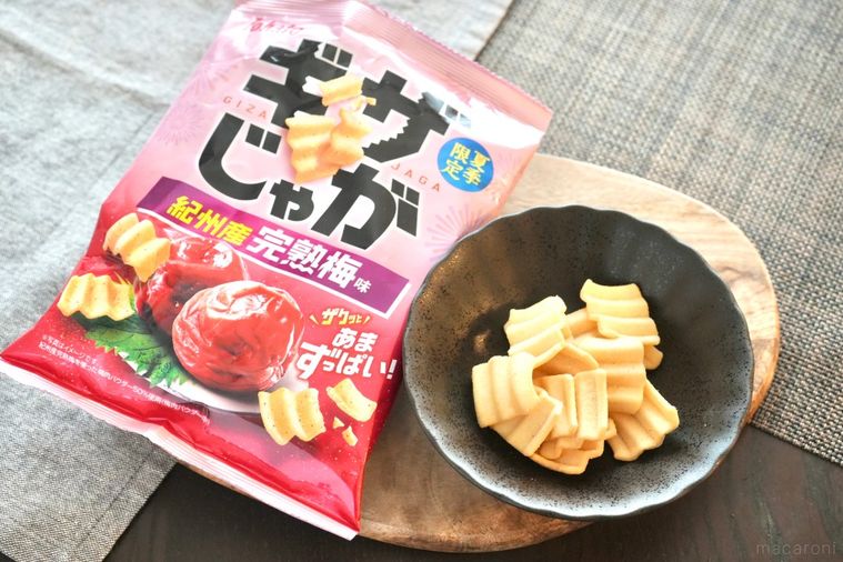 木のカッティングボードと黒い皿にのった梅味のポテトスナックとピンク色のパッケージ