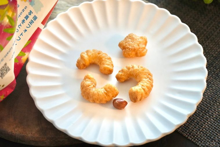 木のカッティングボードと白い皿にのったキャラメルコーンとピーナツと赤ピンク色のパッケージ袋