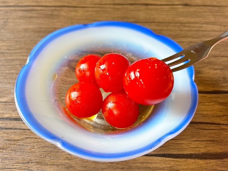 青色のガラスの器に盛られたミニトマトのはちみつ漬けをフォークで食べる様子