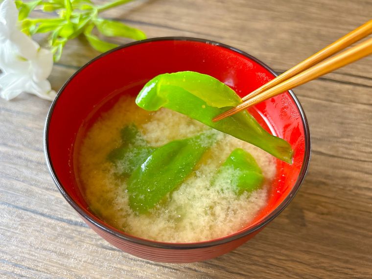 赤色のお椀に盛られたピーマンの味噌汁を食べている様子