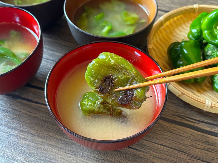 赤色のお椀に盛られたピーマンの味噌汁を食べる様子