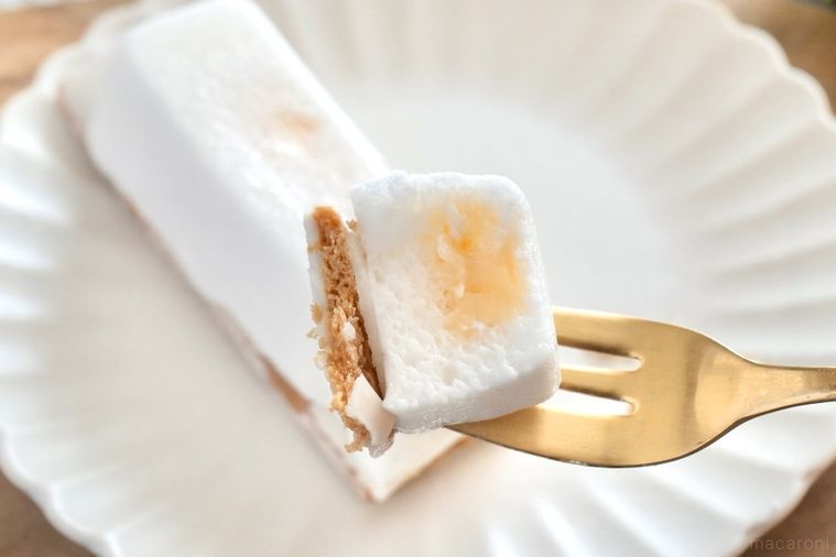 木のカッティングボードと白い皿にのった白いレモン味のスティックケーキを金のフォークで食べる様子