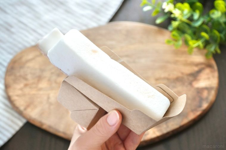 白いレモン味のスティックケーキを持つ手と木のカッティングボードとストライプの布とグリーン