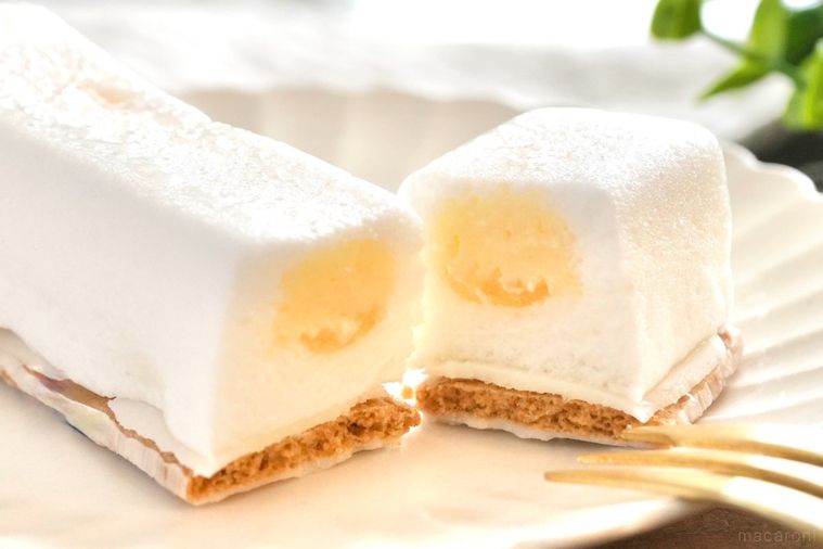 木のカッティングボードと白い皿にのった白いレモン味のスティックケーキの断面と金色のフォーク