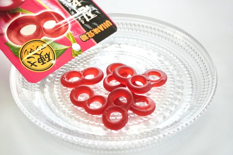 白い背景にチェリー味のグミのピンク色のパッケージとガラスの器と型のグミ