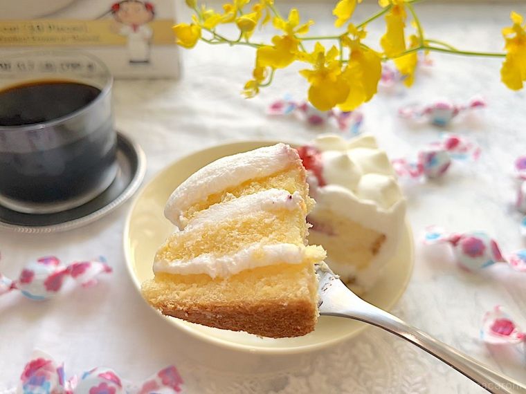 クリーム色の小皿からひと口分フォークですくった不二家のケーキ、ケーキの箱、アイスコーヒー、散らばった不二家のミルキ