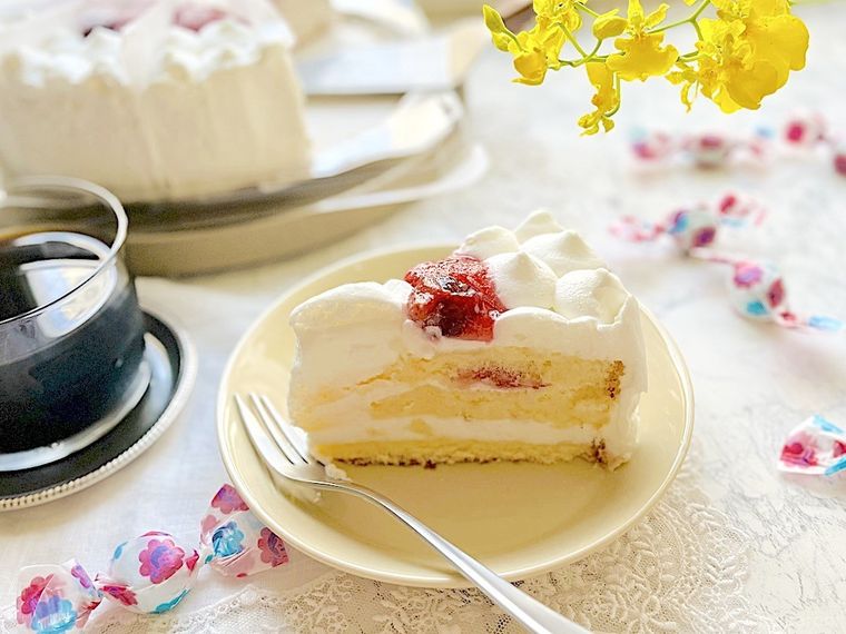 クリーム色の小皿に取り分けてフォークを添えた不二家のケーキとアイスコーヒ、散らばった不二家のミルキー