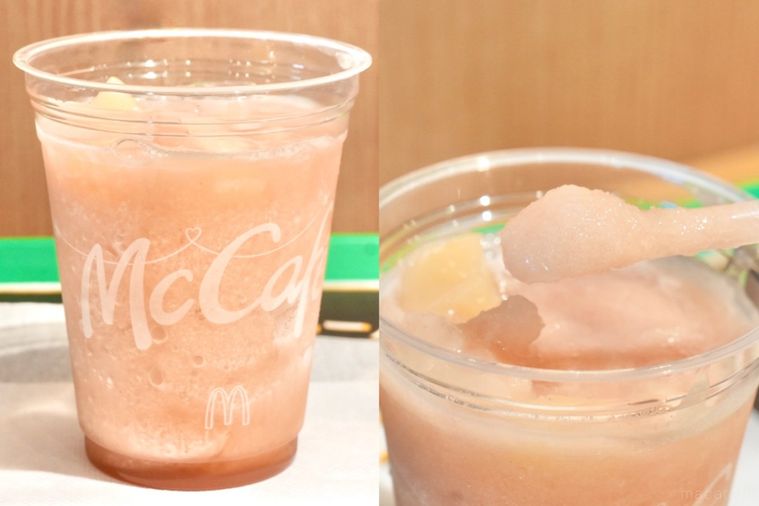 緑色のトレーにのったプラカップ入りの桃味のスムージーをスプーンストローで持ち上げる様子