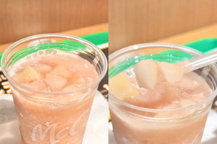 緑色のトレーにのったプラカップ入りの桃味のスムージーから白桃の果肉入りソースをスプーンストローで持ち上げる様子