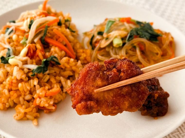 セブンプレミアム ビビンバヤンニョムチキンのヤンニョムチキンを箸で持っている様子