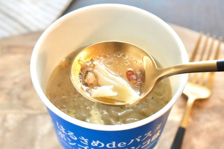 木のカッティングボードにのった青色のカップはるさめパスタボンゴレビアンコ味のスープと金と黒のスプーンとストライプの布