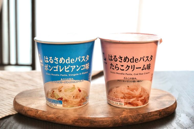木のカッティングボードにのったカップはるさめパスタの青とピンク色のパッケージ