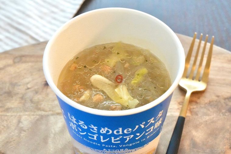 木のカッティングボードにのった青色のカップはるさめパスタボンゴレビアンコ味と金と黒のフォークとストライプの布