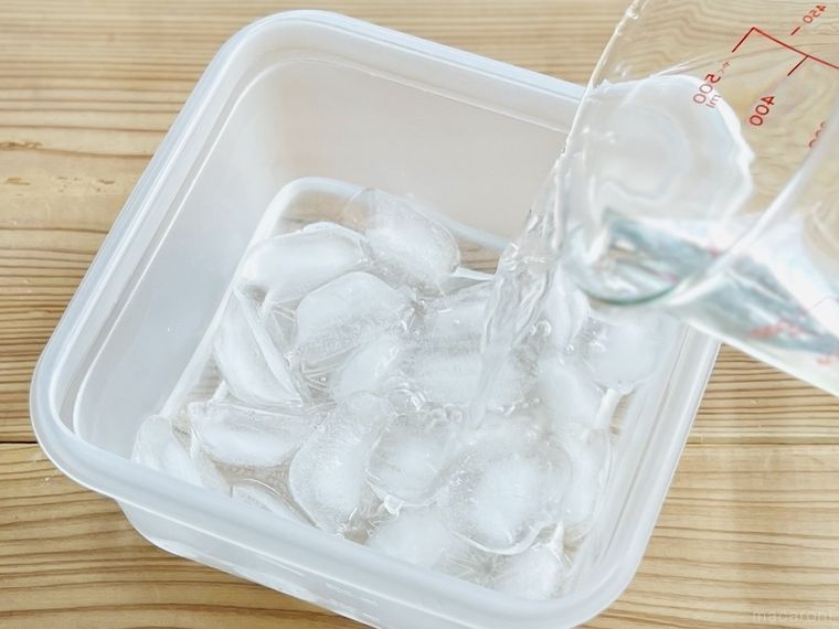 氷と塩が入った保存容器に水をそそいでいる様子