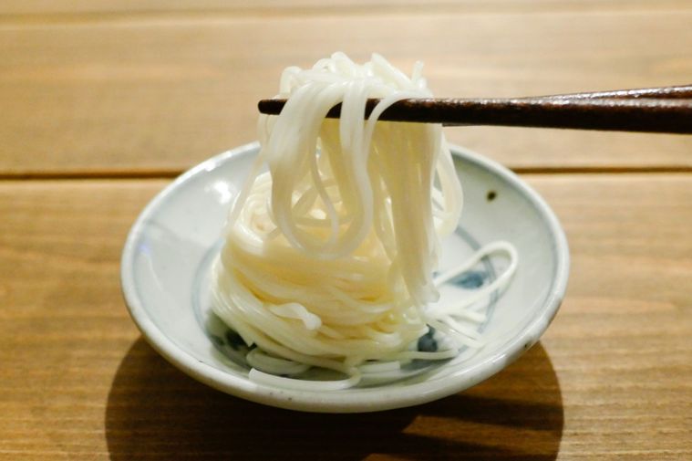 サラダ油を絡めて12時間置いたそうめんを箸で持ち上げる様子