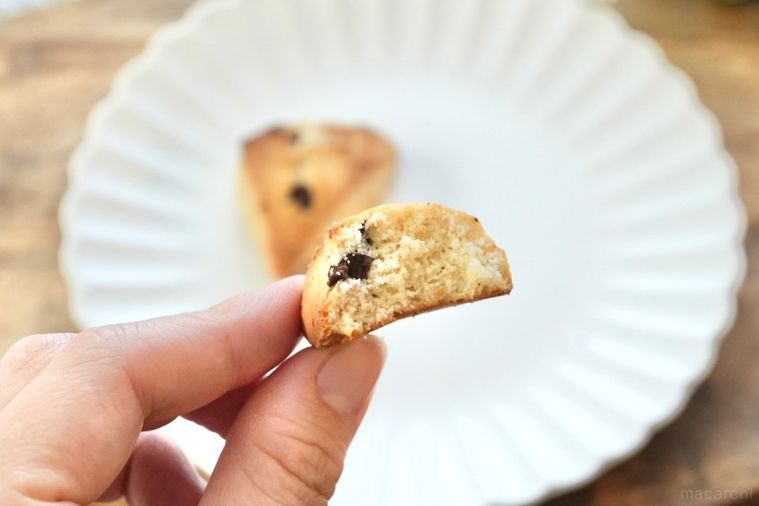 木のカッティングボードと白い皿にのったチョコチャンクスコーンを手に持つ様子