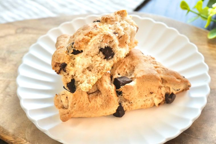 木のカッティングボードと白い皿にのったチョコチャンクスコーンの断面