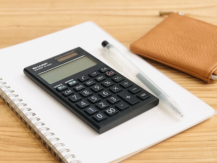 テーブルの上にノート、電卓、ボールペン、お財布が置かれている