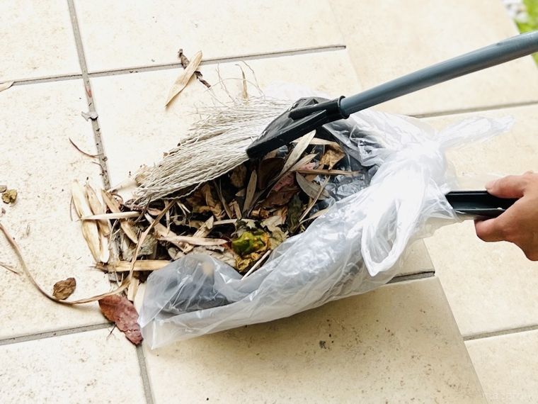 袋をかぶせたちりとりで落ち葉を掃除をしている様子