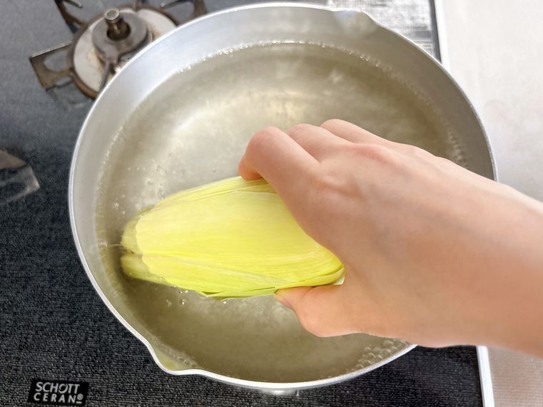 とうもろこしを皮付きのまま鍋に入れる様子