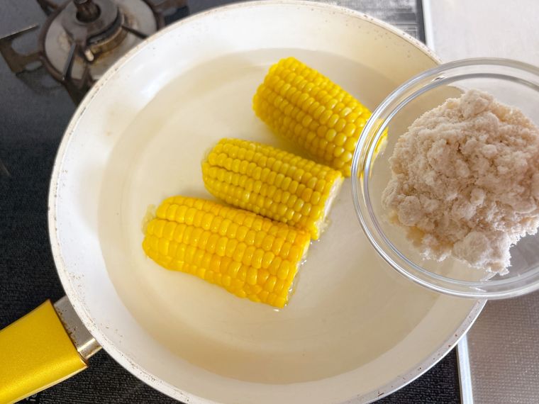 半分にカットしたとうもろこしと水を入れたフライパンにきび砂糖を入れる様子