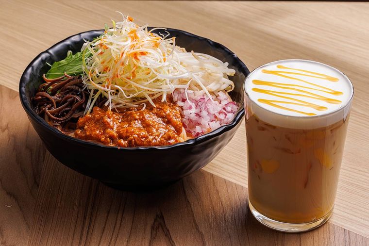 木製のテーブルの上に、タムジャイサムゴーの汁なし麻辣担々米線とマンゴー茉莉花ミルクティーが並んでいる