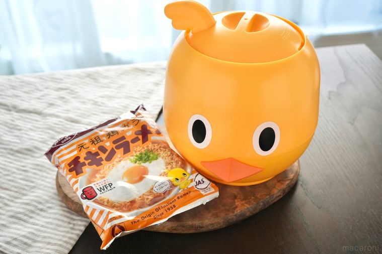 木のカッティングボードにのったひよこ型のガジェットとラーメンの袋とストライプの布
