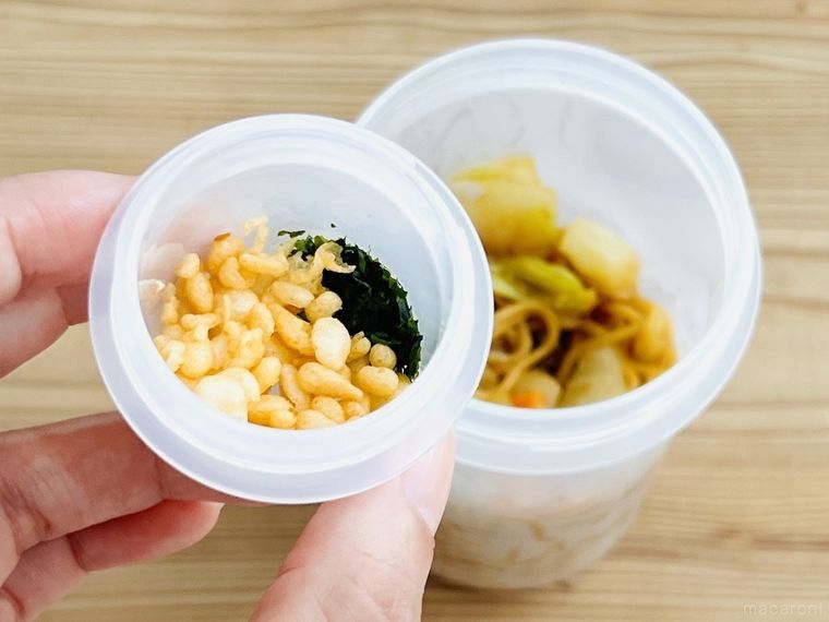 焼きそばが入ったトッピングカップ付き ランチカプセルに天かすと青のりを入れようとしている様子