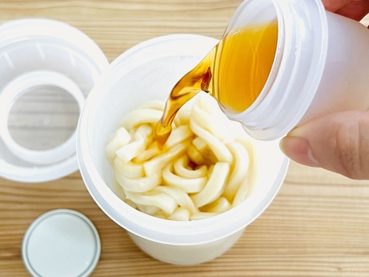 うどんが入ったトッピングカップ付き ランチカプセルにつゆをかけている様子