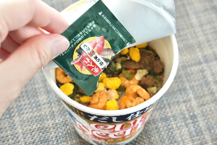 茶色いランチョンマットとだし仕込カップヌードルにだしの袋を入れる様子