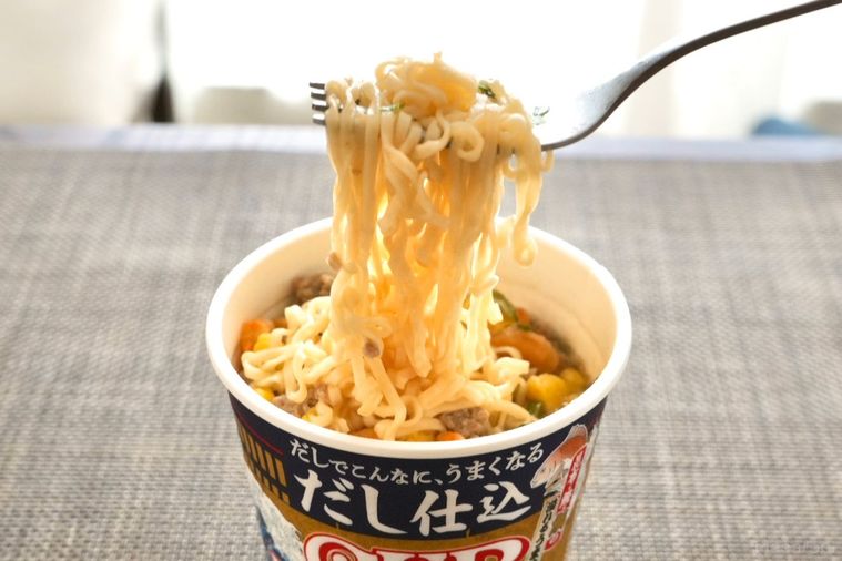 だし仕込カップヌードルの麺を銀のフォークで持ち上げて食べる様子