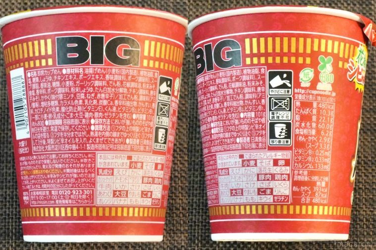 茶色いランチョンマットにのった赤色のパッケージのカップヌードル花椒香るシビ辛麻婆ビッグの原材料表示とカロリー表示