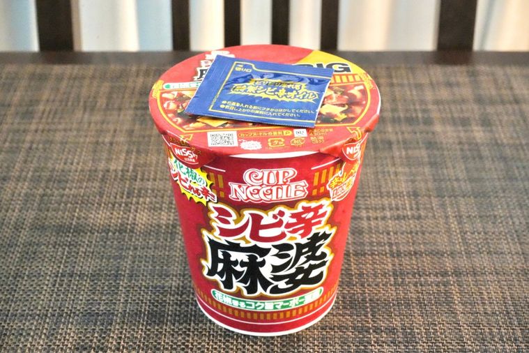 茶色いランチョンマットにのった赤色のパッケージのカップヌードル花椒香るシビ辛麻婆ビッグ