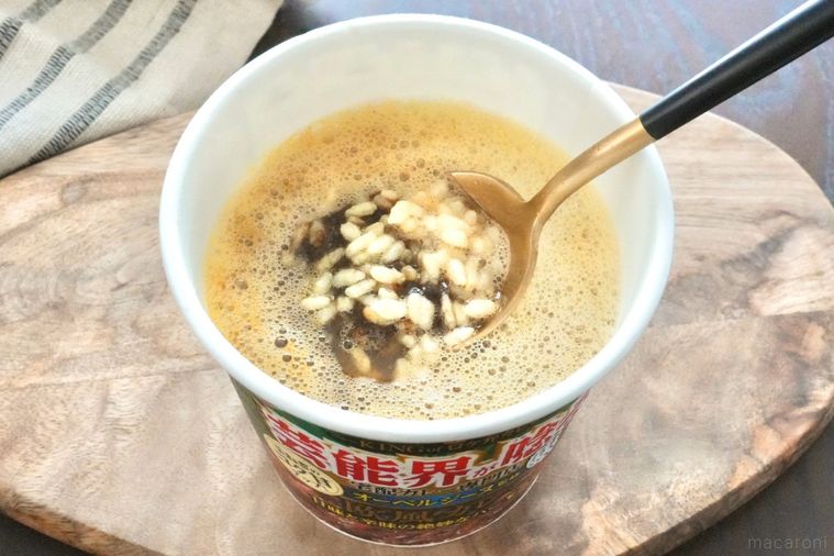 木のカッティングボードにのったカレーカップメシを黒と金のスプーンでかき混ぜる様子