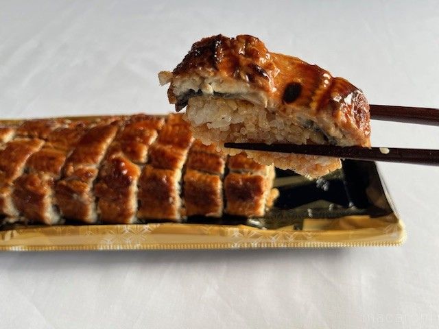 鰻の蒲焼がのった寿司をハシで一切れ持ち上げている