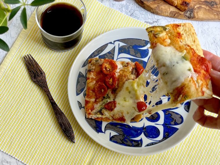 焼いたピンサマルゲリータの端を持ち上げ、とろけたチーズが伸びている様子