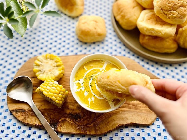 コストコのコーンブレッドロールをコーンスープに浸しているところ、輪切りにしたコーン2個、スプーン